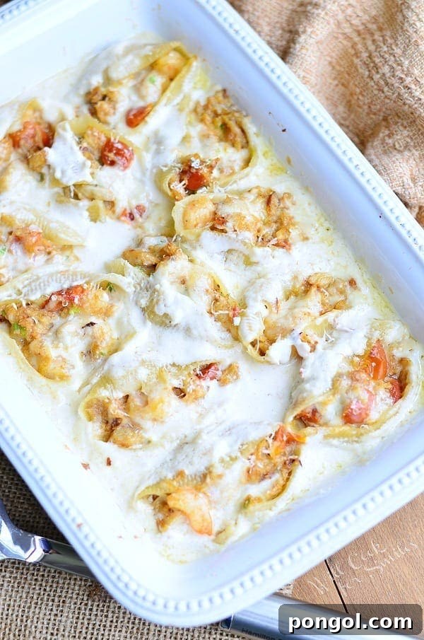 A large white casserole dish filled with generously stuffed pasta shells, bathed in a rich Alfredo sauce and ready for serving.
