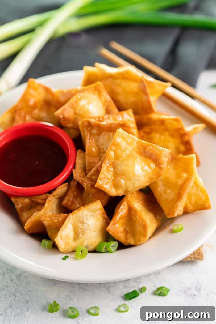 A white plate adorned with perfectly fried crab rangoon, accompanied by chopsticks and a small red dipping bowl.