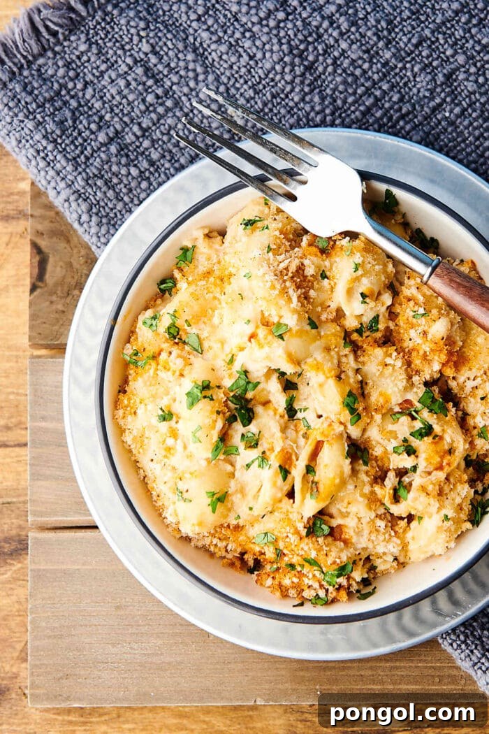A white bowl of creamy mac and cheese, topped with golden breadcrumbs and garnished with fresh herbs.