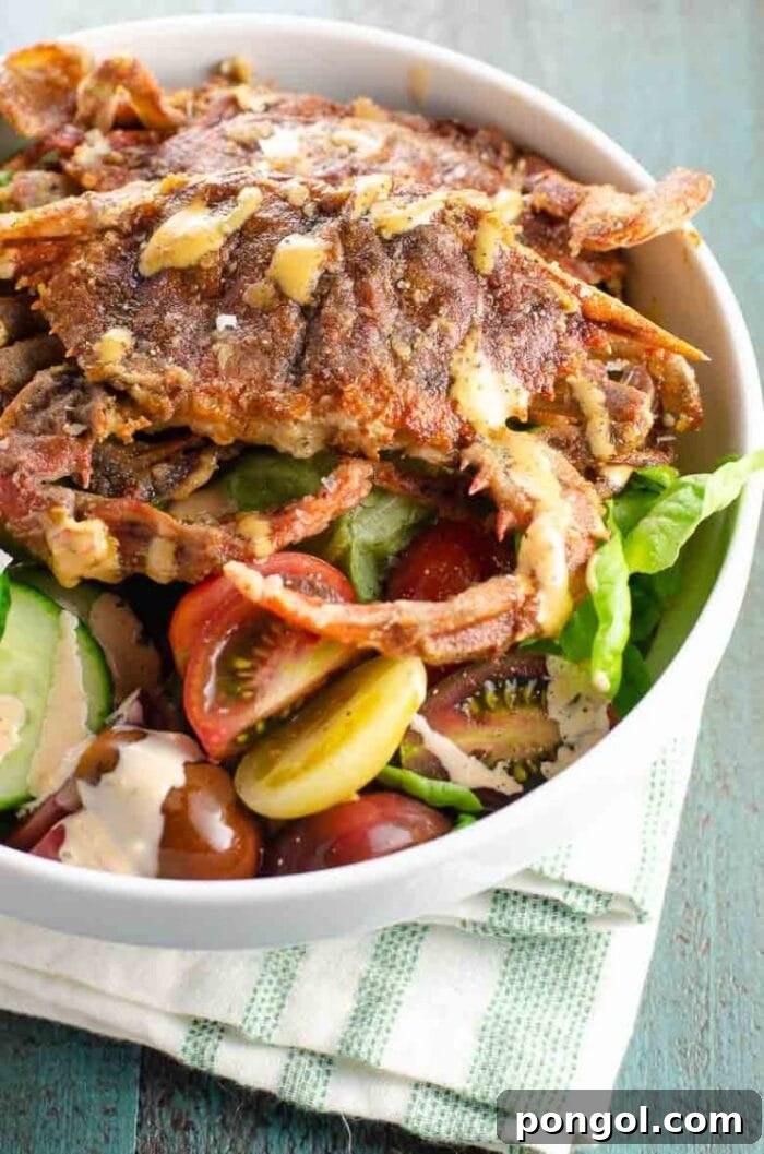 Crispy fried soft shell crab arranged on a vibrant salad in a large white bowl, drizzled with spicy sauce.
