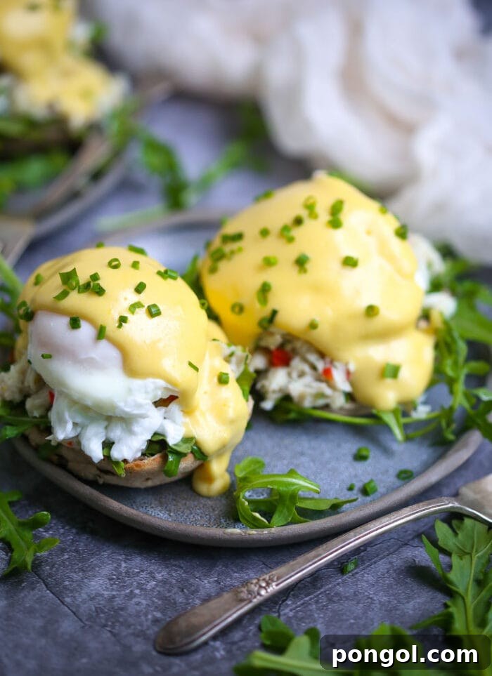 Two exquisitely prepared eggs benedict with crab, served on a blue plate with a subtle grey trim.