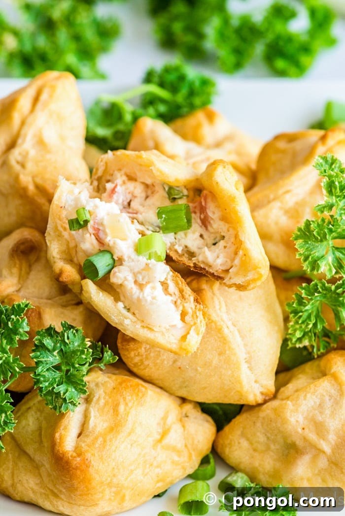 A perfectly fried crescent roll torn in half, revealing a luscious cream cheese and crab filling.