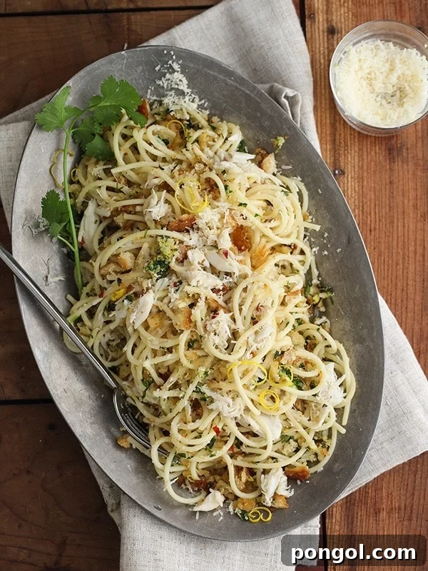 A dark silver oval-shaped platter brimming with spaghetti and generous chunks of crab, garnished with fresh herbs.