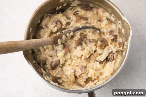 Creamy Wild Mushroom Risotto 12 Sautéed mushrooms being carefully stirred into a large silver saucepan of creamy risotto with a wooden spoon, blending seamlessly.
