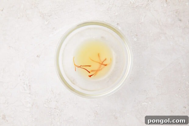 Creamy Wild Mushroom Risotto 7 A small glass bowl containing warm chicken stock with vibrant saffron threads infusing, preparing to add unique color and flavor to the risotto.