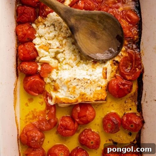 Baked feta and tomatoes smushed in oil in a large pan with a wooden spoon
