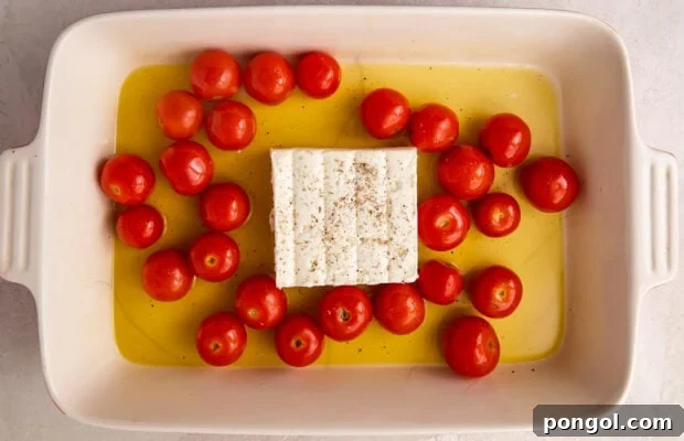 Cherry tomatoes and feta in a pool of olive oil in a rectangular baking dish, ready for the oven.