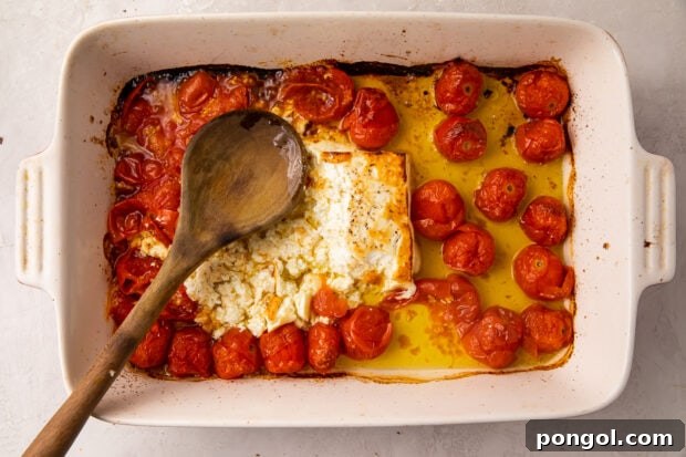 Baked feta and tomatoes in a casserole dish, after roasting, with some browning on the feta.