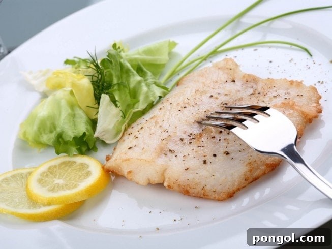 Grilled orange roughy on a white plate with lemon slices and a small salad, presenting a light and healthy meal arrangement.