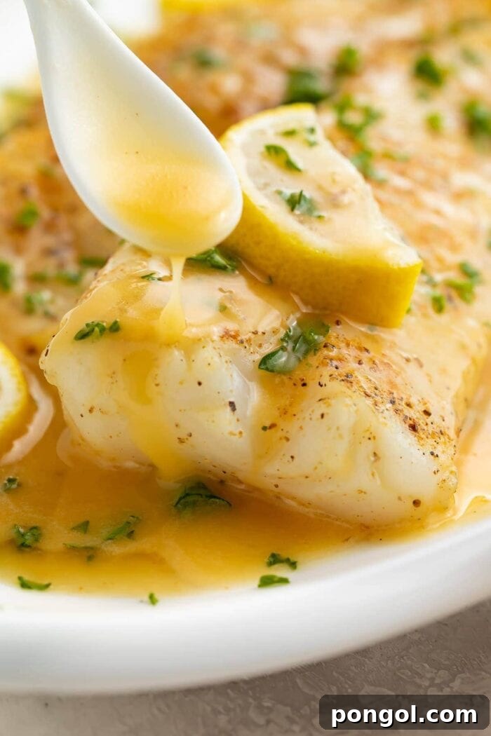 Golden lemon butter sauce drizzled generously over a perfectly cooked fish fillet on a white platter, garnished with fresh herbs.