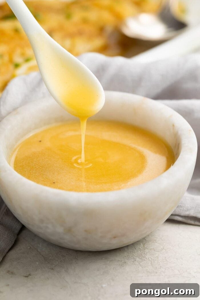 Close-up of a spoon drizzling golden brown butter lemon sauce into a rustic stone bowl, showing its smooth, rich texture.