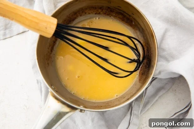 Lemon butter sauce in a silver saucepan with a black whisk