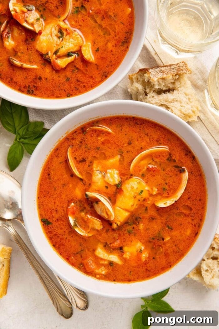 Two bowls of red Italian fish stew on a table surrounded by pieces of bread