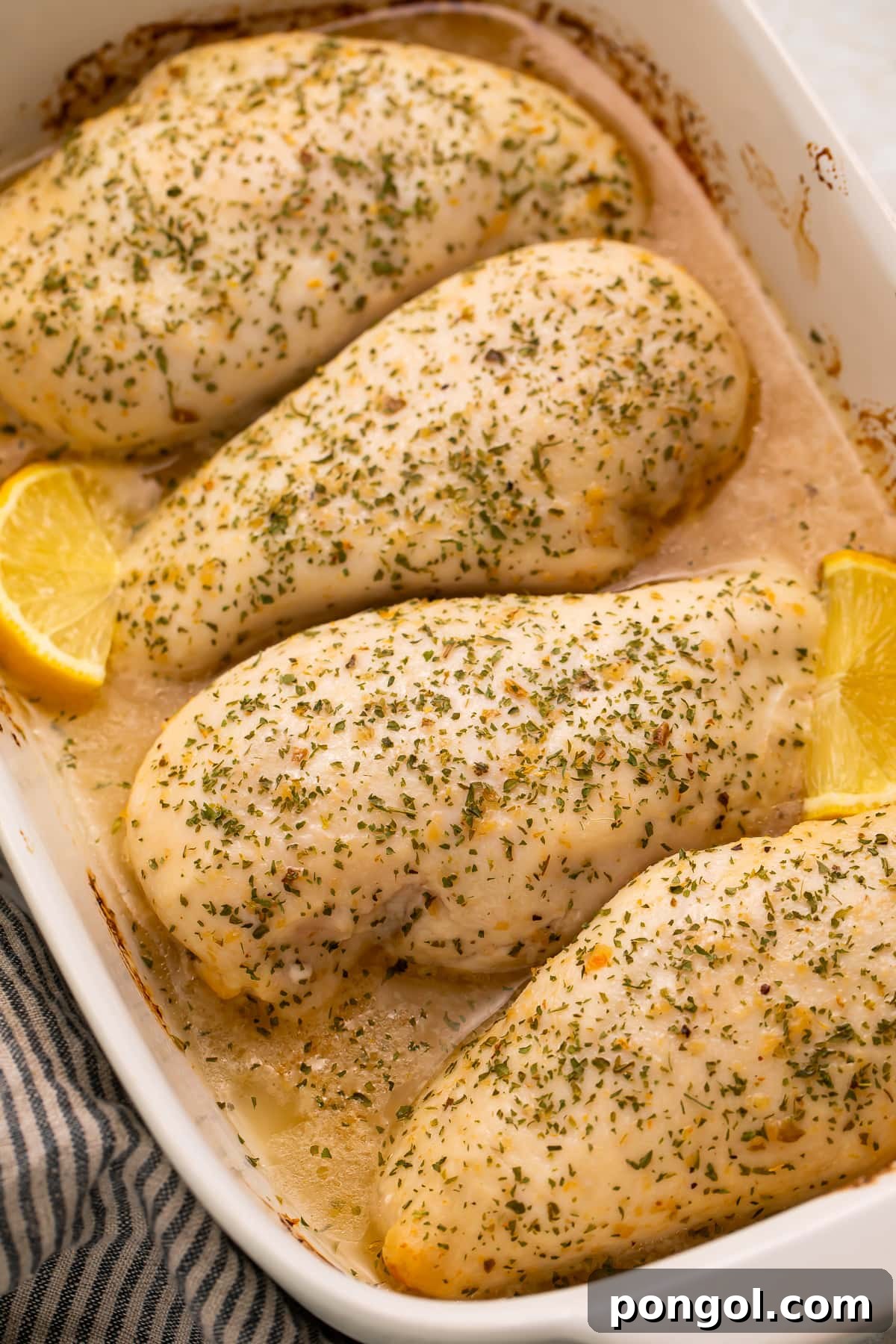 4 large chicken breasts baked with Italian dressing and garnished with lemon wedges in a large baking dish.