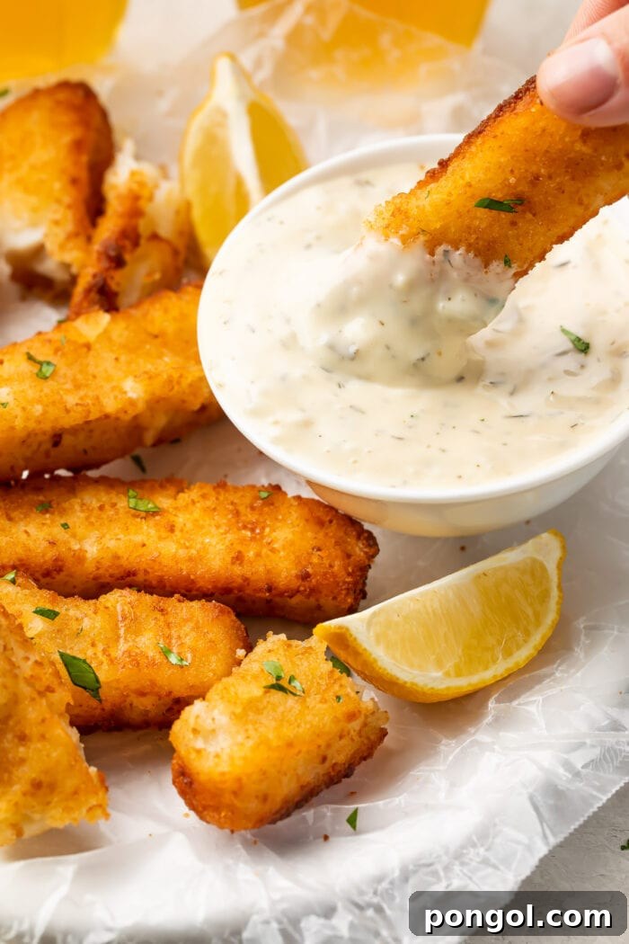 A close up of an air fried fish stick being dipped into a small bowl of dipping sauce 