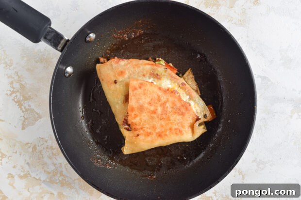 A freshly folded Mexican crunchwrap cooking in a hot skillet until golden brown and crispy