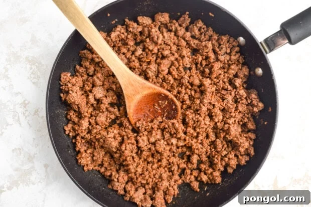 Cooked ground beef seasoned with taco seasoning, simmering in a large skillet