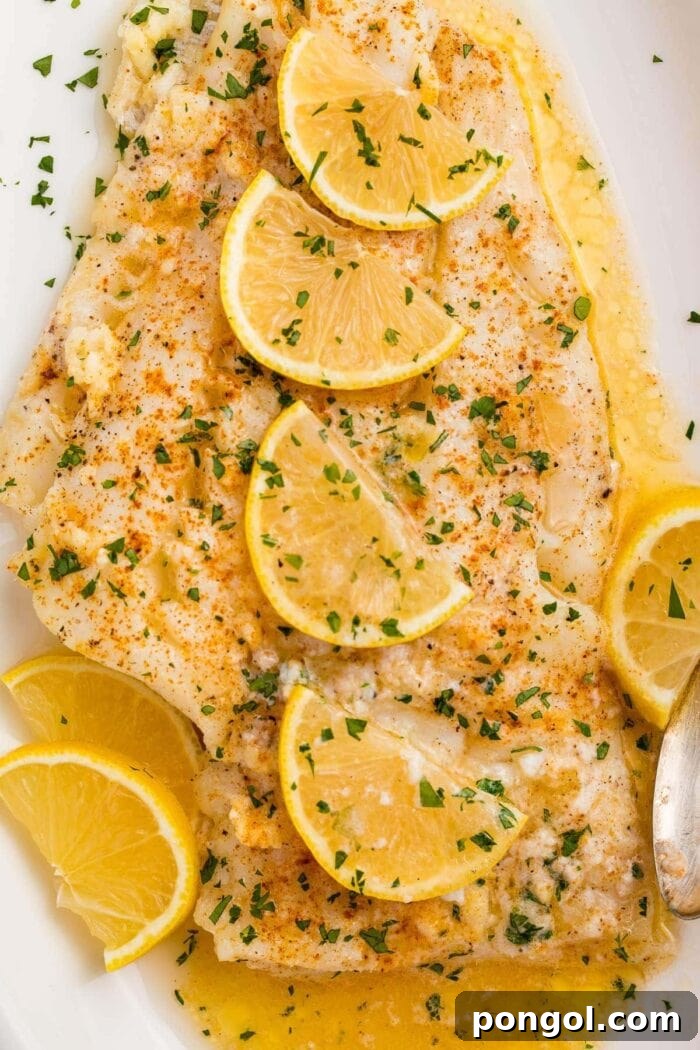 Baked fish with lemon garlic butter sauce and slices of lemon on a white platter