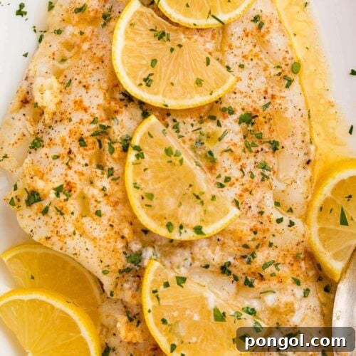 Baked fish with lemon garlic butter sauce and slices of lemon on a white platter