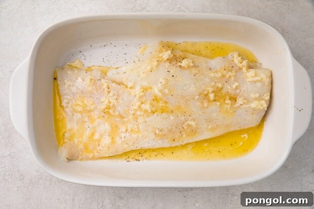 Uncooked fish in a baking dish, covered with lemon-garlic butter