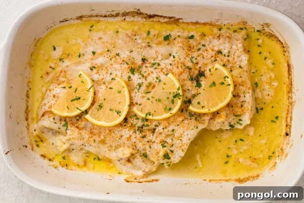 Baked fish topped with parsley and lemon slices in a white baking dish