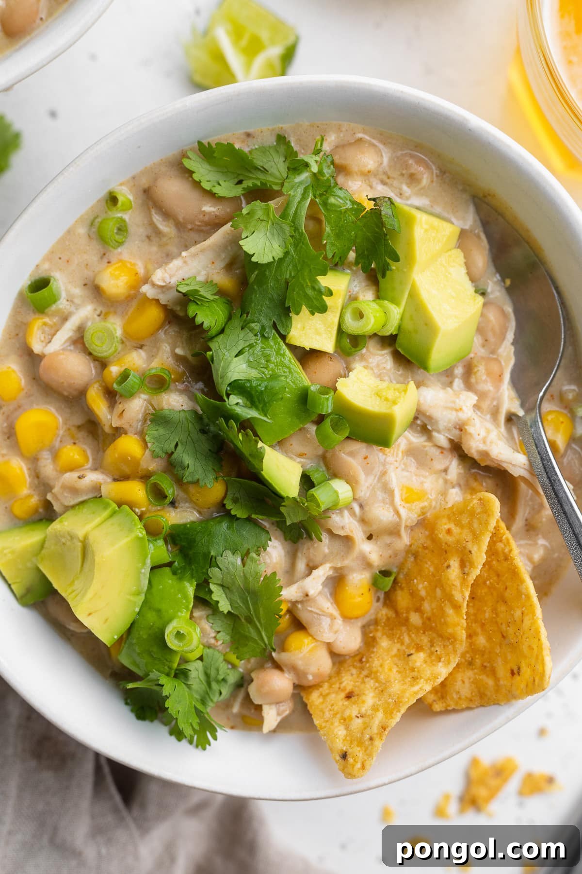 Overhead view of a bowl of white chicken chili, cooked in the Instant Pot, with avocado, cilantro, and tortilla chips.
