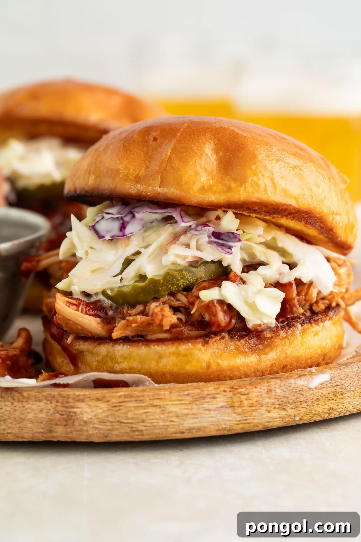 Crockpot-cooked pulled BBQ chicken on a sandwich bun with pickle chips and coleslaw.