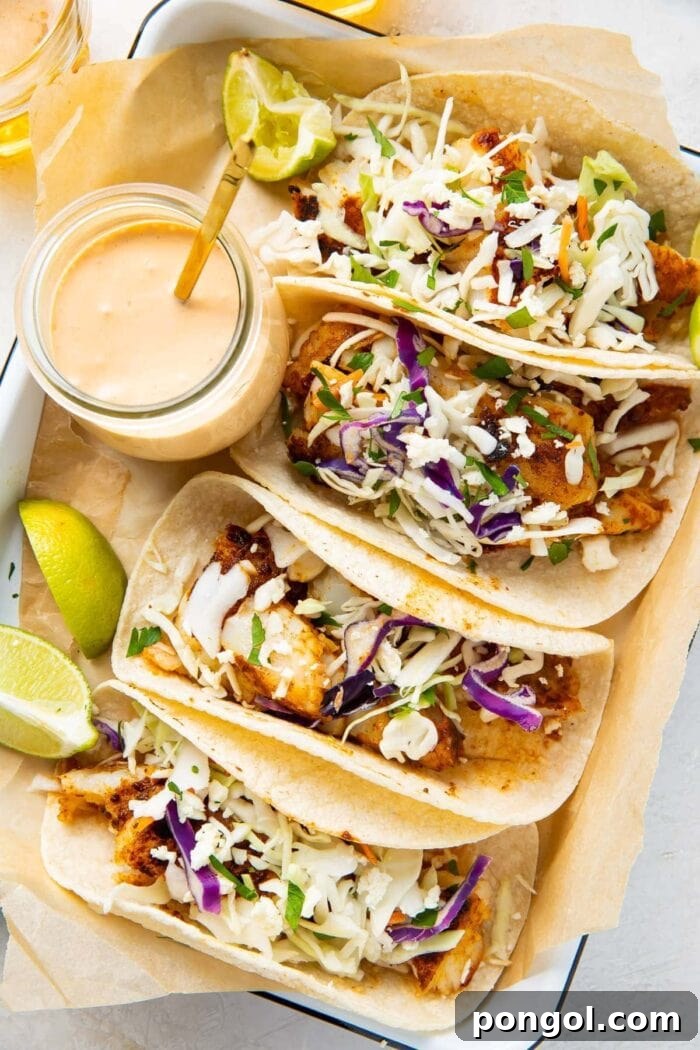 Four mouth-watering fish tacos neatly arranged on a platter, accompanied by a glass jar filled with the irresistible fish taco sauce