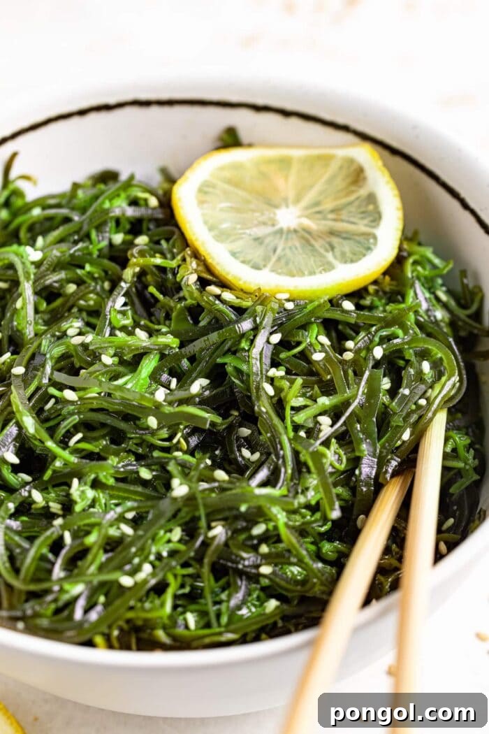 A vibrant bowl of homemade seaweed salad topped with sesame seeds and a lemon slice, ready to be enjoyed with chopsticks.