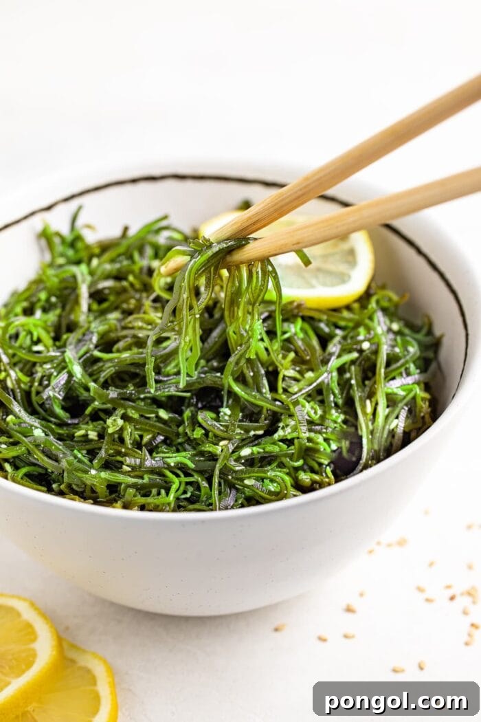 A close-up shot of seaweed salad being lifted from a bowl with chopsticks, highlighting its fresh texture.
