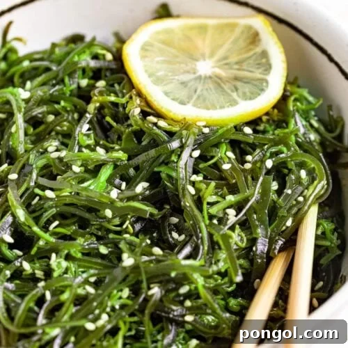A beautiful seaweed salad in a bowl with chopsticks, garnished with sesame seeds and a lemon slice.