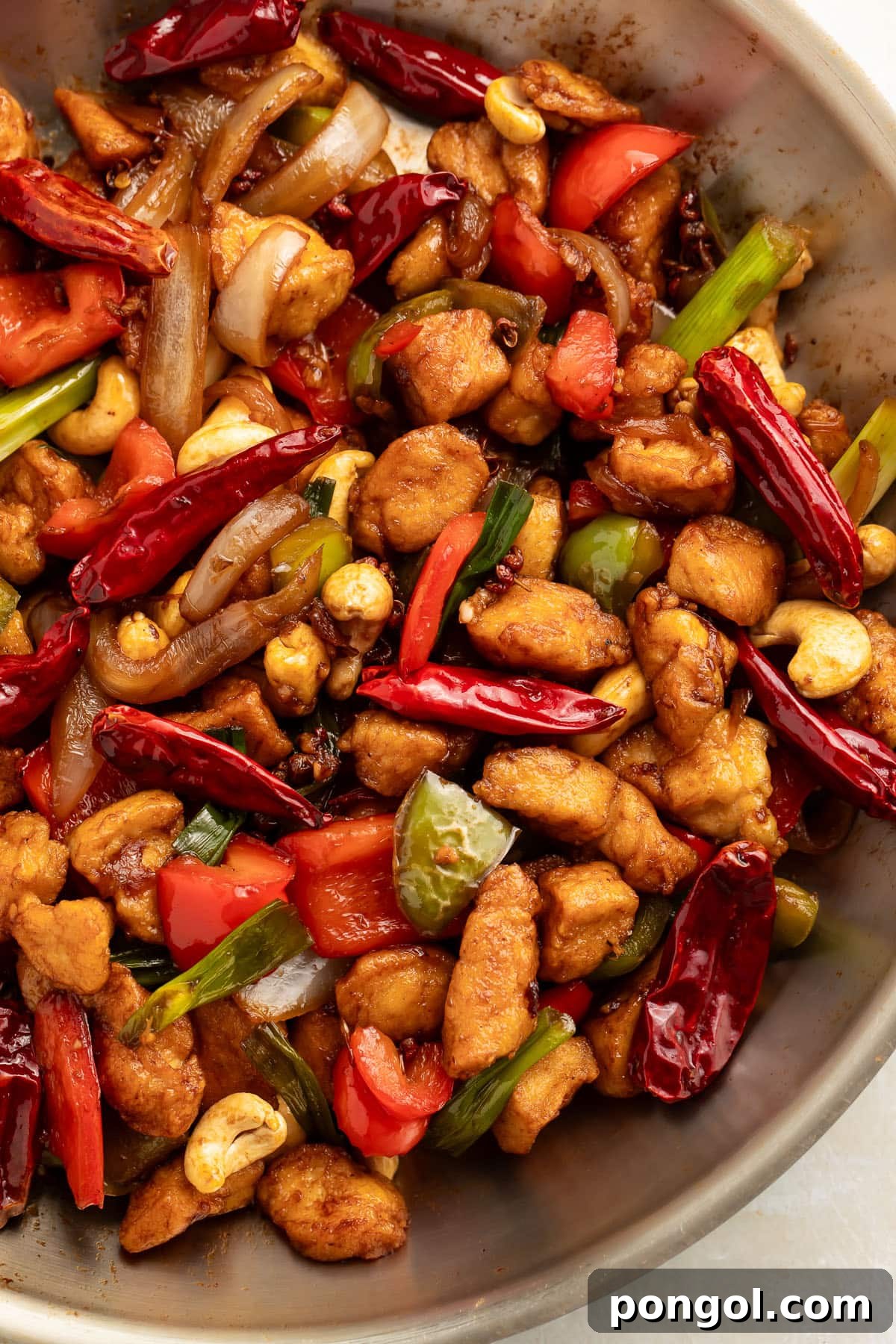 Top-down view of a large wok holding prepared Szechuan chicken with cashews, chilies, peppercorns, and chicken. A vibrant, aromatic dish ready to be served.