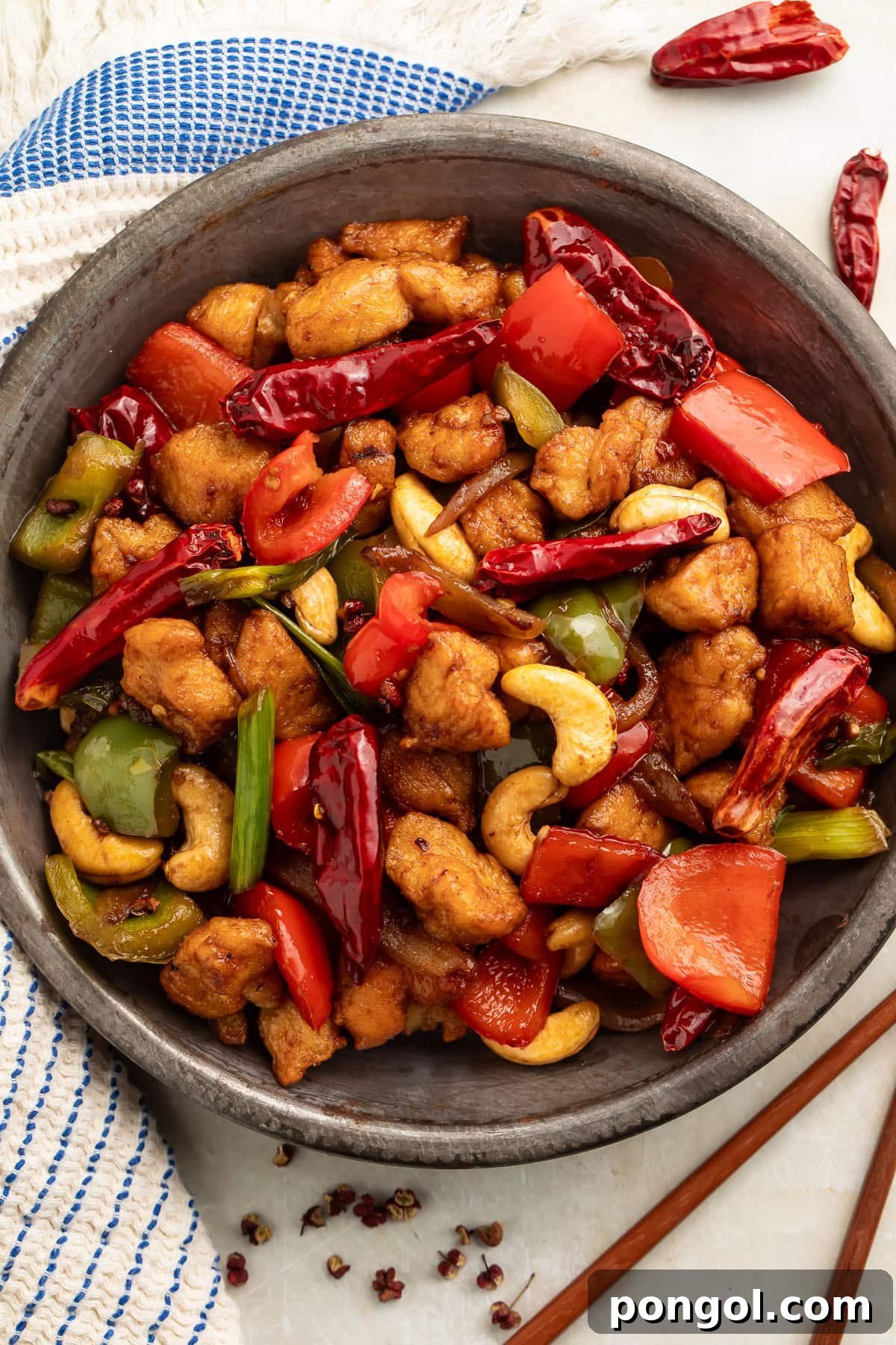 A bowl of Szechuan chicken on a table with chopsticks. The dish looks appetizing and ready to eat.