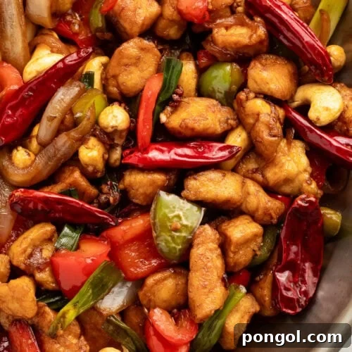 Top-down view of a large wok holding prepared Szechuan chicken with cashews, chilies, peppercorns, and chicken.