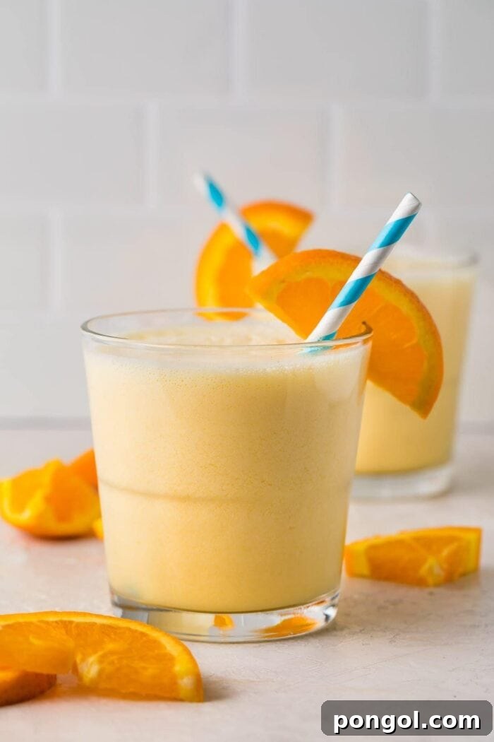 Short glass containing a serving of Orange Julius with an orange slice and a blue and white striped straw