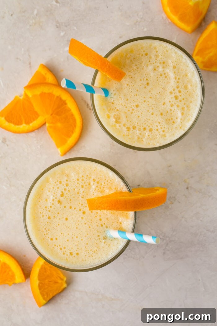 Overhead image of two glasses of Orange Julius with orange wedge garnishes and blue and white striped straws