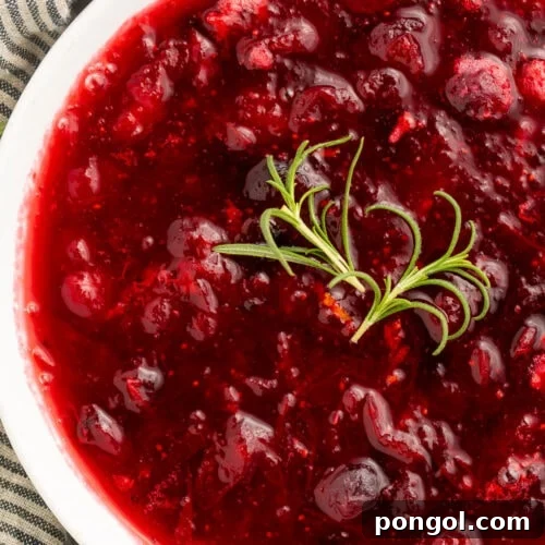 Close-up of whole berry rosemary cranberry sauce in a white bowl with a garnish of fresh rosemary.