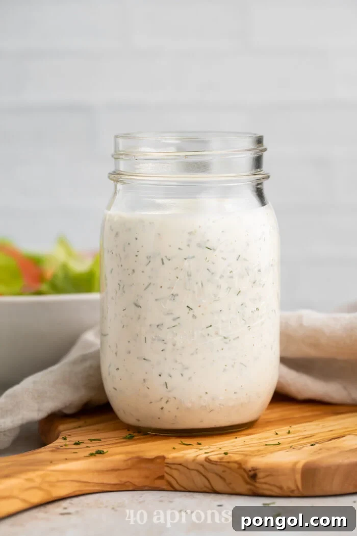 Side view of a mason jar filled with homemade buttermilk ranch dressing, sitting on a wooden serving board.