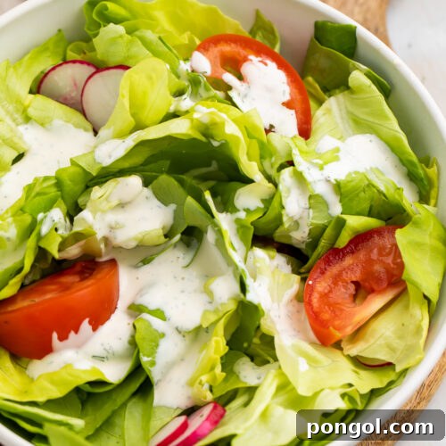 Overhead, angled view of a house salad with buttermilk ranch dressing and large slices of tomatoes.