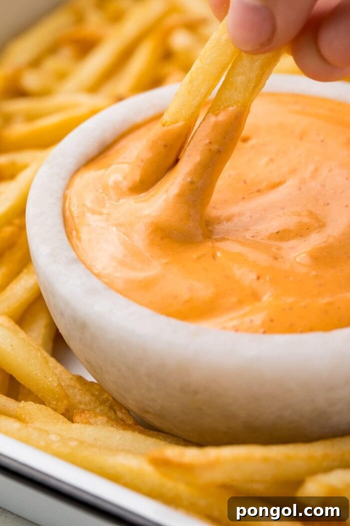Two french fries dipped in chipotle aioli in a small bowl