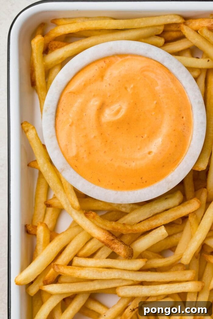 A small marble bowl of chipotle aioli surrounded by french fries on a baking sheet
