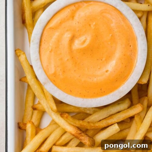 A small marble bowl of chipotle aioli surrounded by french fries on a baking sheet