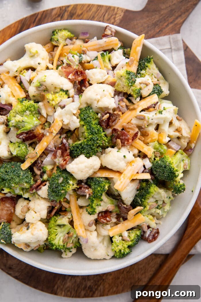 A bowl of broccoli cauliflower salad on a wooden cutting board, ready to be served.