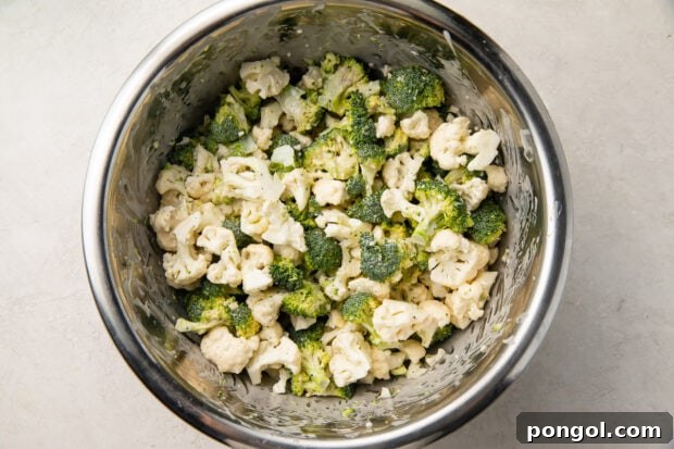 Broccoli and cauliflower florets in a large mixing bowl with dressing.