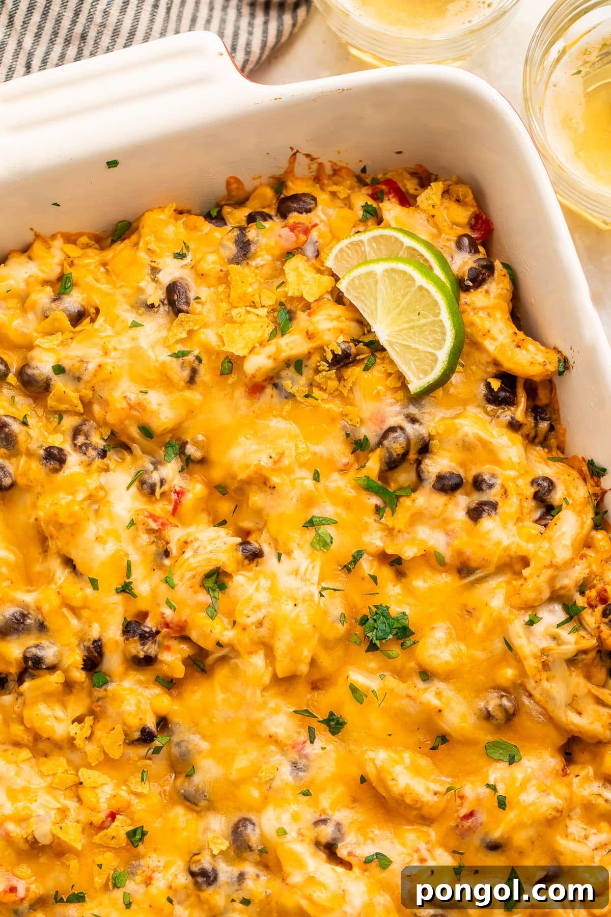 Mexican Chicken Extravaganza 7 Overhead view of a casserole dish holding a Mexican chicken casserole topped with melted cheese and two lime wedges.