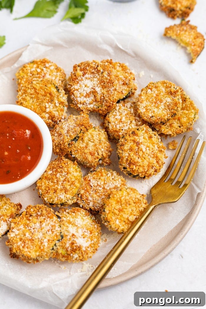Crispy Air Fryer Zucchini Chips on a plate, generously sprinkled with Parmesan cheese and served alongside a bowl of vibrant marinara sauce.