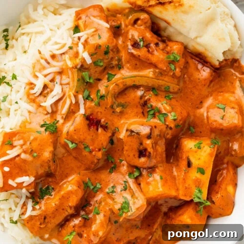 Deep orange paneer tikka masala in a white bowl with white rice and a piece of naan.