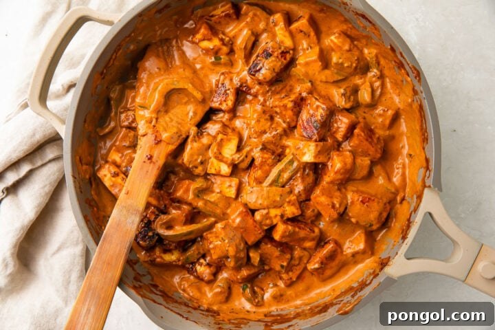 Paneer tikka masala in a large skillet with a large wooden spoon.