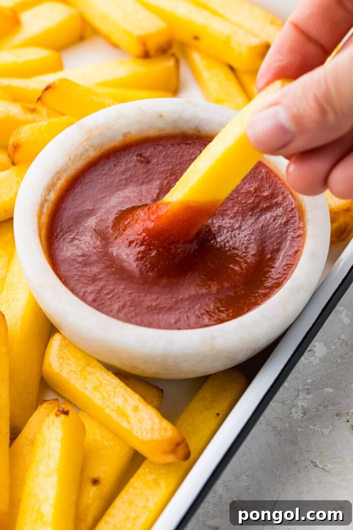 A crispy fry being dipped into a small bowl of rich keto ketchup.