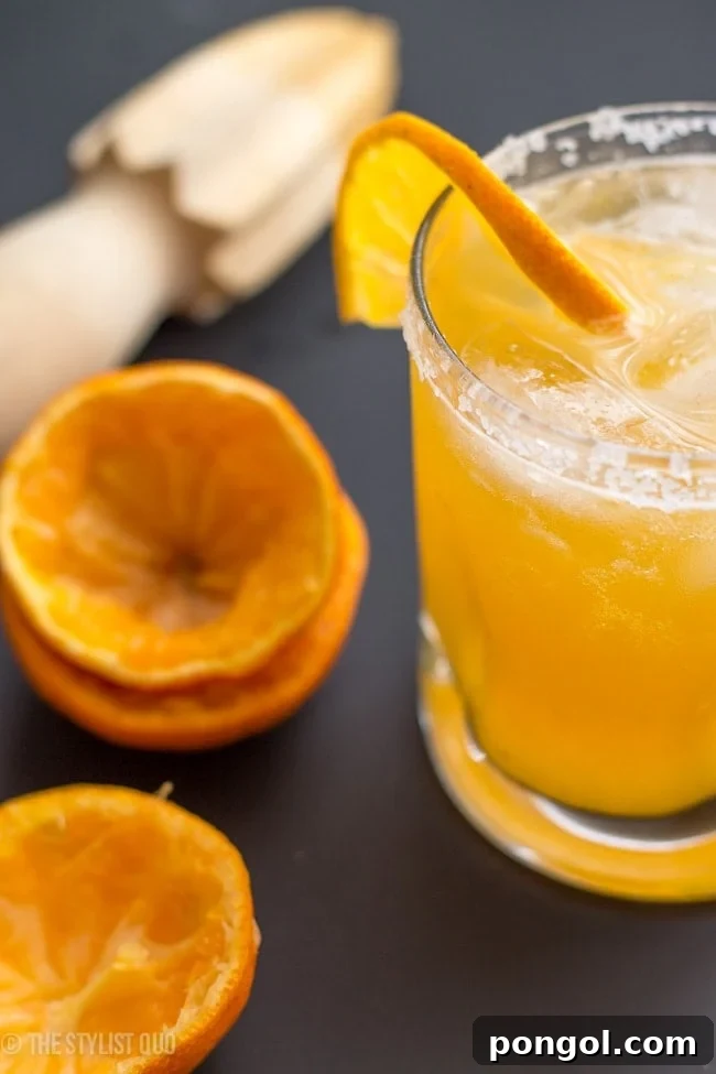 A close-up of a Clementine Margarita with ice, garnished with a clementine slice and a salted rim, ready to be enjoyed.